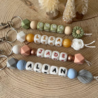 Porte-clés personnalisé en perles de silicone avec prénom, aux couleurs naturelles, présenté sur un fond en bois.