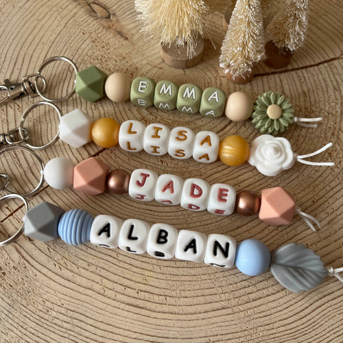 Porte-clés personnalisé en perles de silicone avec prénom, aux couleurs naturelles, présenté sur un fond en bois.