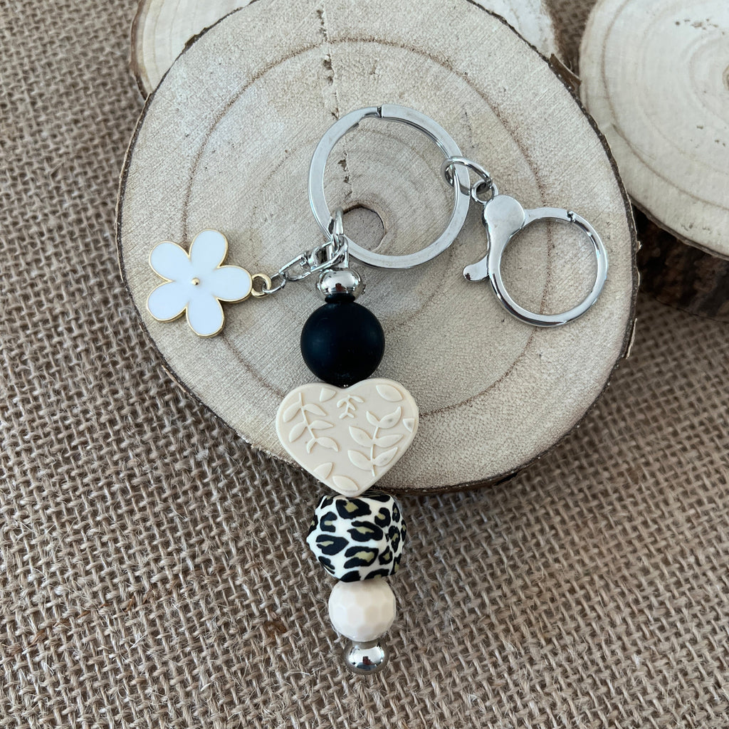 Porte-clés femme en perles de silicone avec pendentif cœur texturé, fleur blanche et perle léopard, création artisanale.