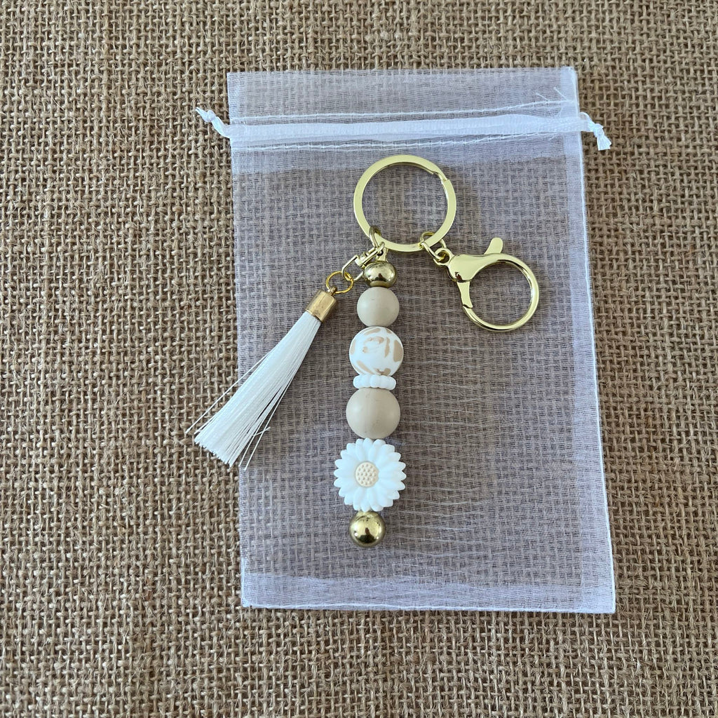 Porte-clés femme artisanal avec fleur marguerite, perles neutres et breloque dorée, accessoire élégant et tendance.