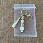 Porte-clés femme artisanal avec fleur marguerite, perles neutres et breloque dorée, accessoire élégant et tendance.