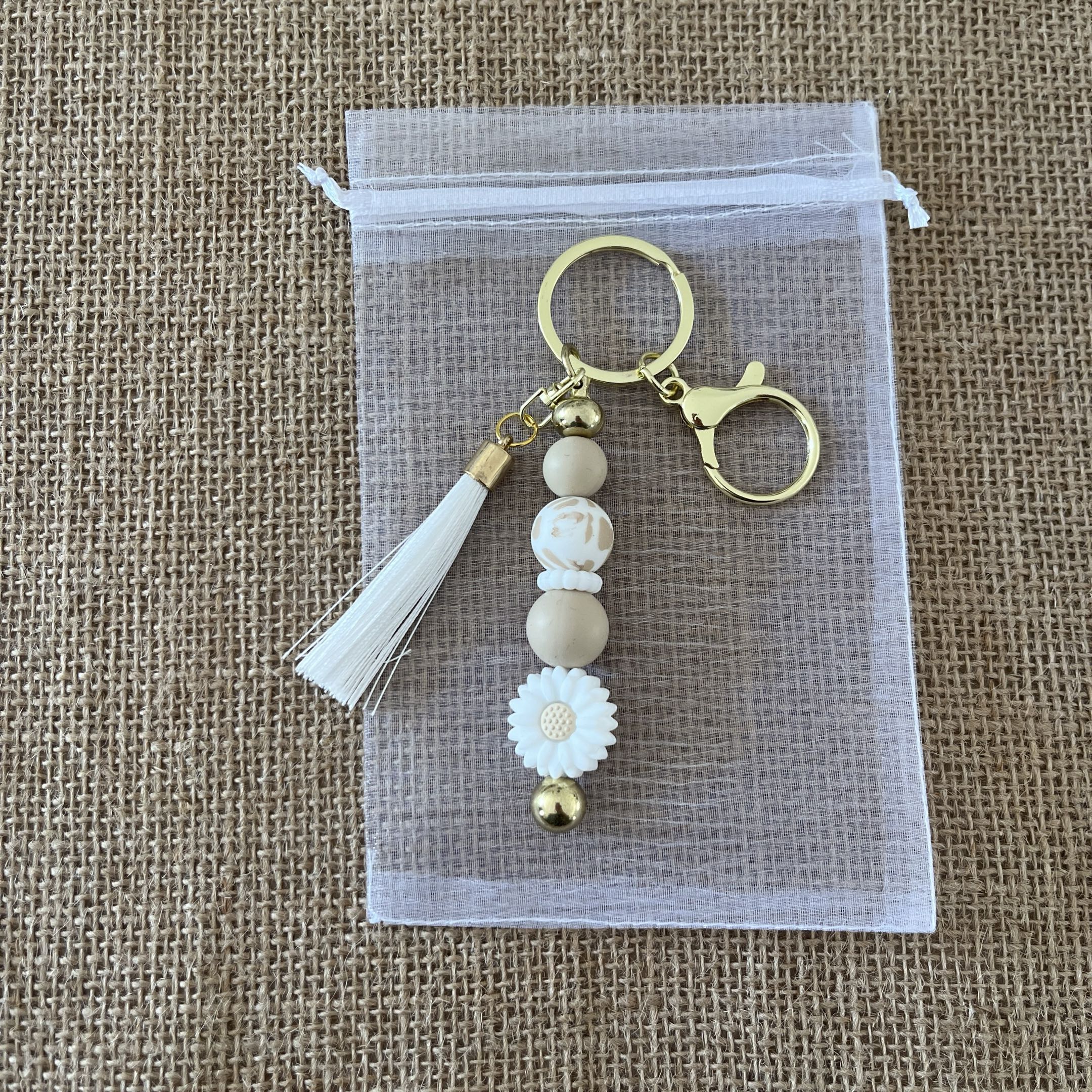 Porte-clés femme artisanal avec fleur marguerite, perles neutres et breloque dorée, accessoire élégant et tendance.